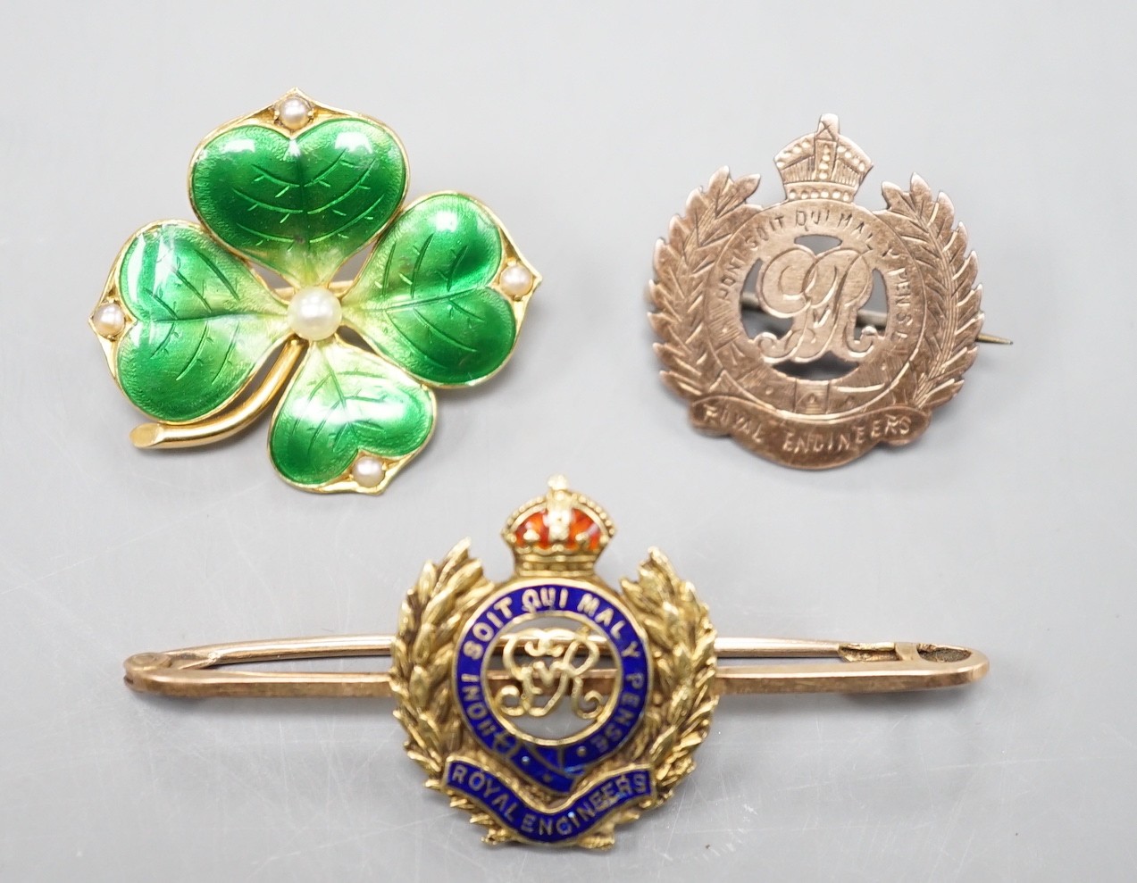 An early 20th century and two colour enamel set Royal Engineers sweetheart brooch, 5cm, gross 5.6 grams, an 18ct, seed pearl and green enamel clover brooch, 26mm, gross 6.2 grams and a sterling and yellow metal brooch.